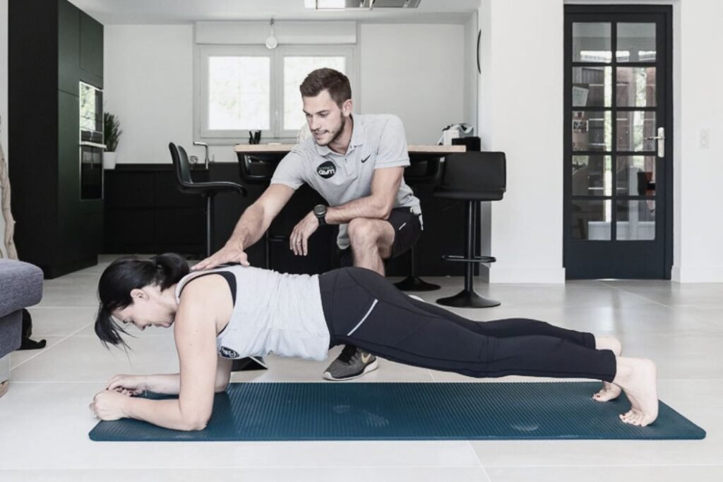 Un coach sportif Domicil'Gym aide sa cliente à réaliser un exercice de gainage.