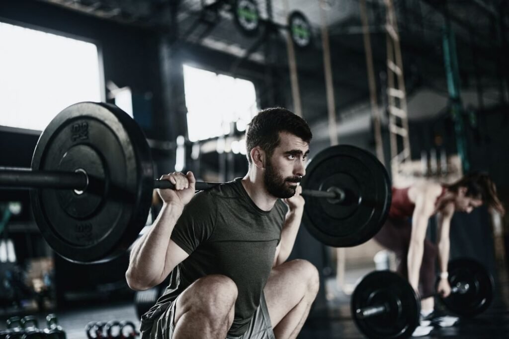 Un homme fait des squats en salle de sport sous la supervision de son coach sportif.